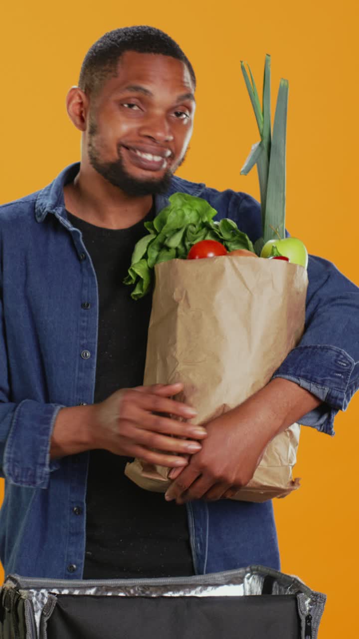 Uomo afroamericano sorridente che mette alimenti freschi in un sacchetto di carta