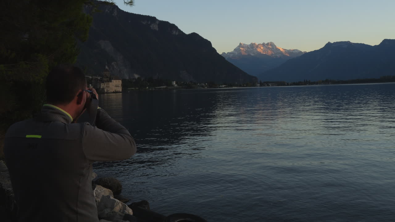 Uomo di mezza età fotografa il castello di Chillon in Svizzera durante l'ora d'oro.