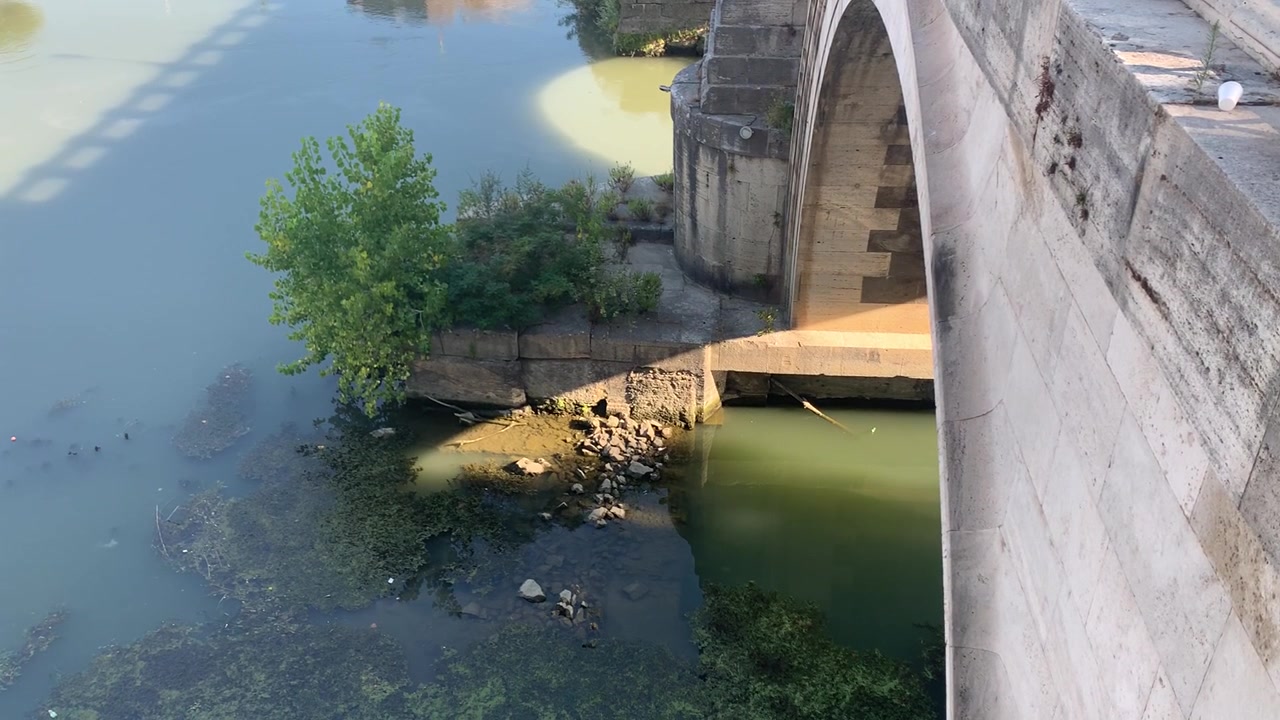 Antik bir Roma köprüsünün kemerlerinin altından nazikçe akan Tiber Nehri'nin suyu.