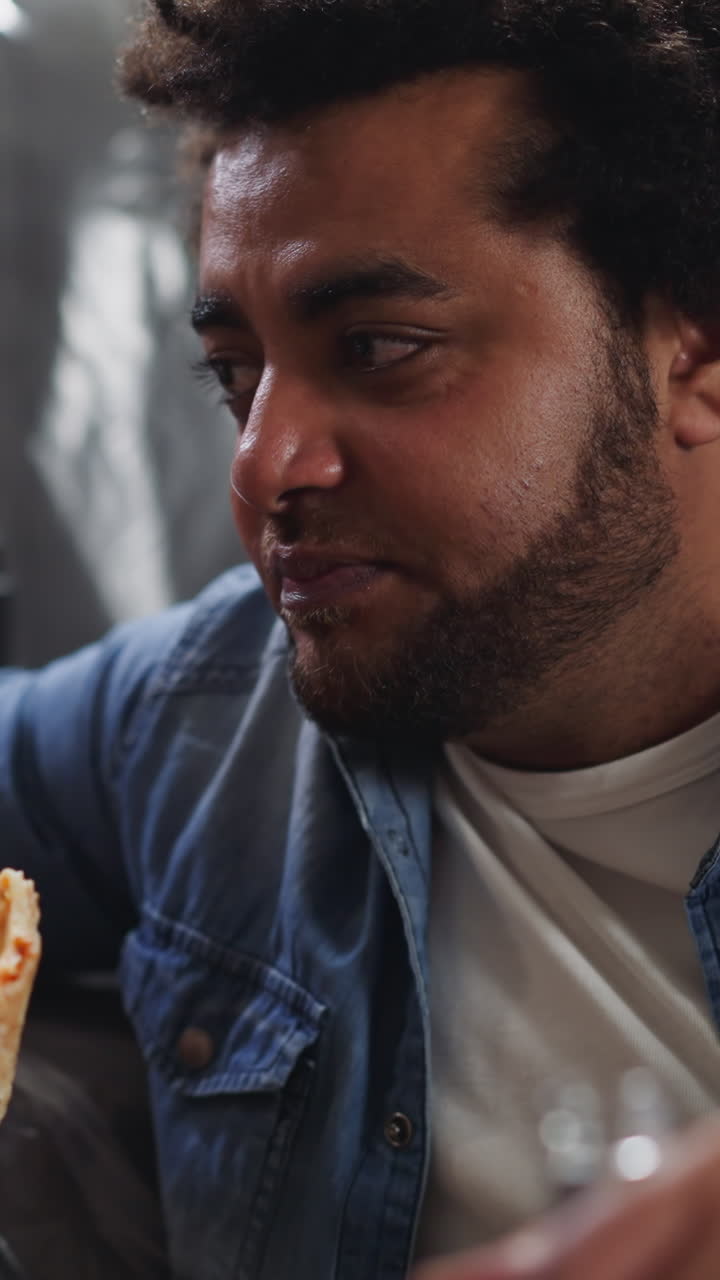 Bearded man talks to colleague eating pizza near sofa covered with plastic closeup. Constructors rest and drink beer in studio