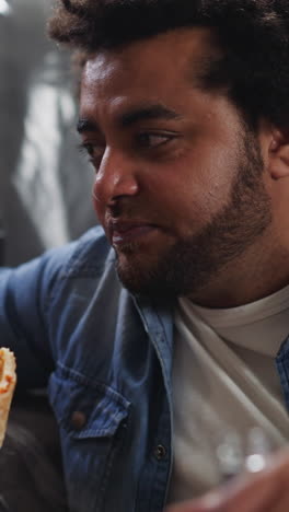 bearded man talks to colleague eating pizza near sofa covered with plastic closeup. constructors rest and drink beer in studio