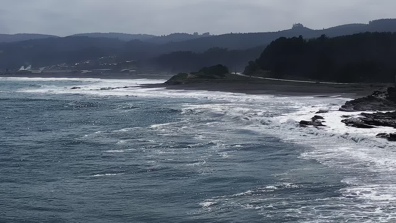 Cloudy day at the ocean shore in Chile with waves and distant hills