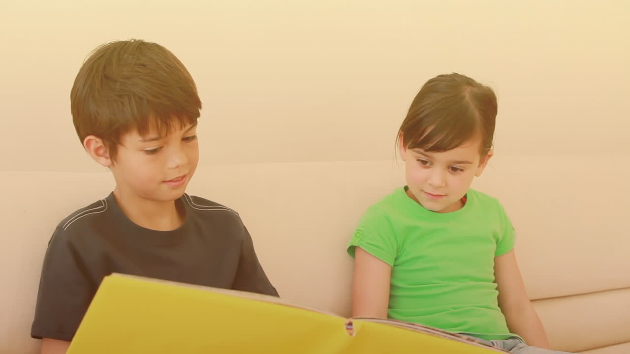 백인 형제가 집에서 여동생에게 책을 읽고 있습니다.