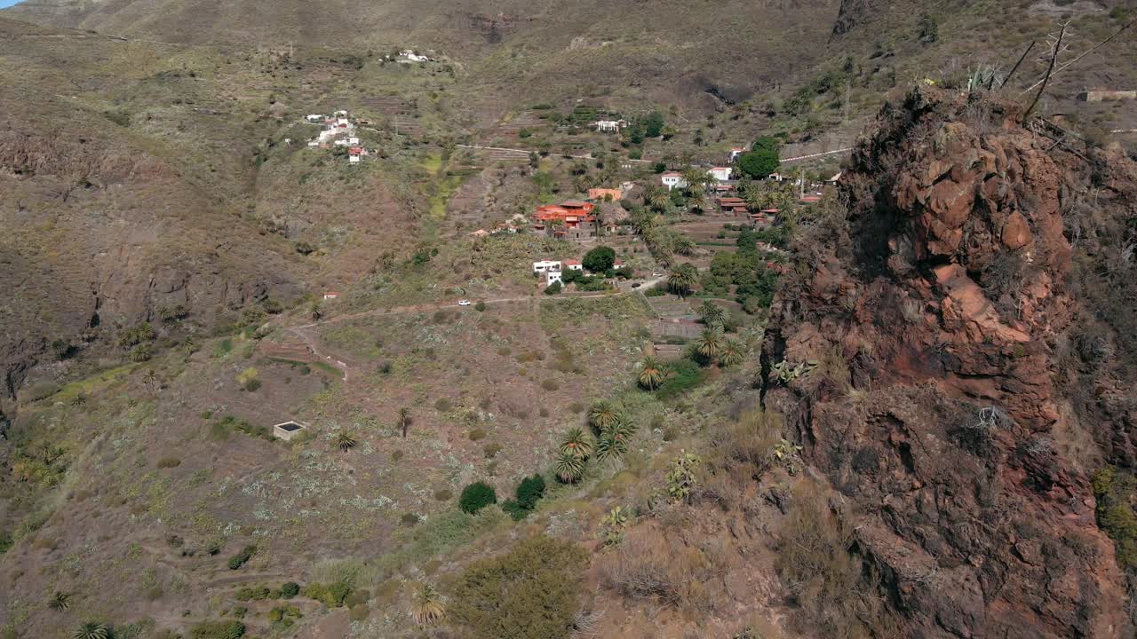 revelando una toma de arco de un pequeño pueblo de montaña detrás de una gran roca roja, una toma aérea