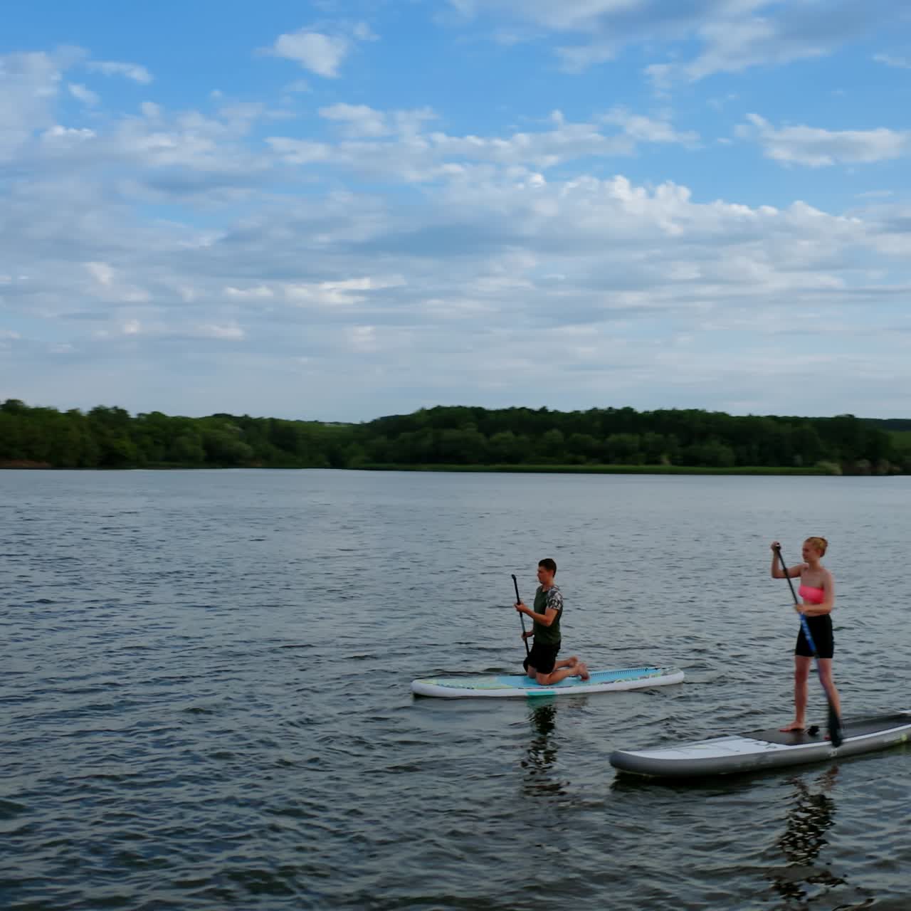People spend time on water in the evening. Young man and woman sailing on river on boards with oar in summer at dusk. Orbital view
