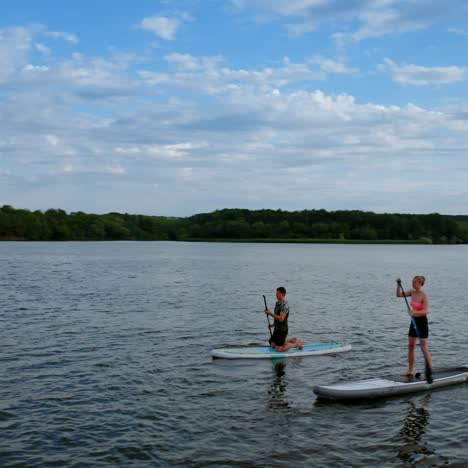 people spend time on water in the evening. young man and woman sailing on river on boards with oar in summer at dusk. orbital view