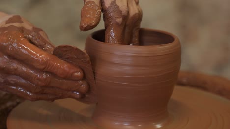 old woman potter working on potter wheel making a clay pot. master forming the clay with her hands creating pot in a workshop