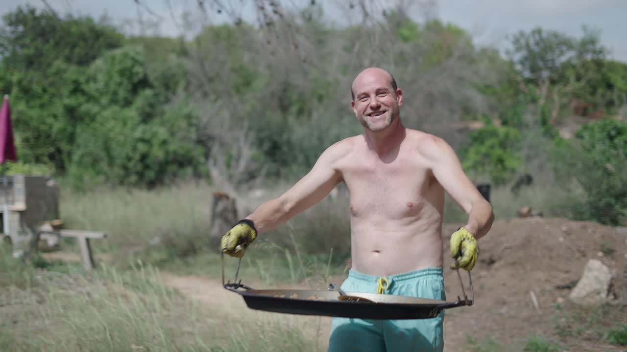A man carrying a paella pan in a rural outdoor setting