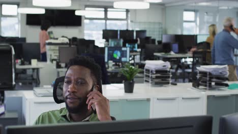 man talking on smartphone while sitting on his desk at office