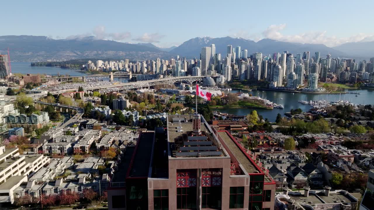 Canadian Flag Waving On Building Rooftop With View Of Downtown Vancouver, Granville Bridge, And False Creek In Background. wide aerial shot