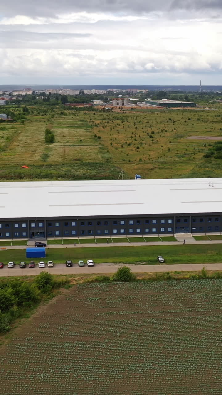 Aerial panorama of a modern plant. Exterior of a large commercial warehouse situated among green fields. Camera moves forward. Vertical video