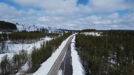 aerial drone shot of a car driving on a highway road in between remote, picturesque coniferous woodlands in sweden