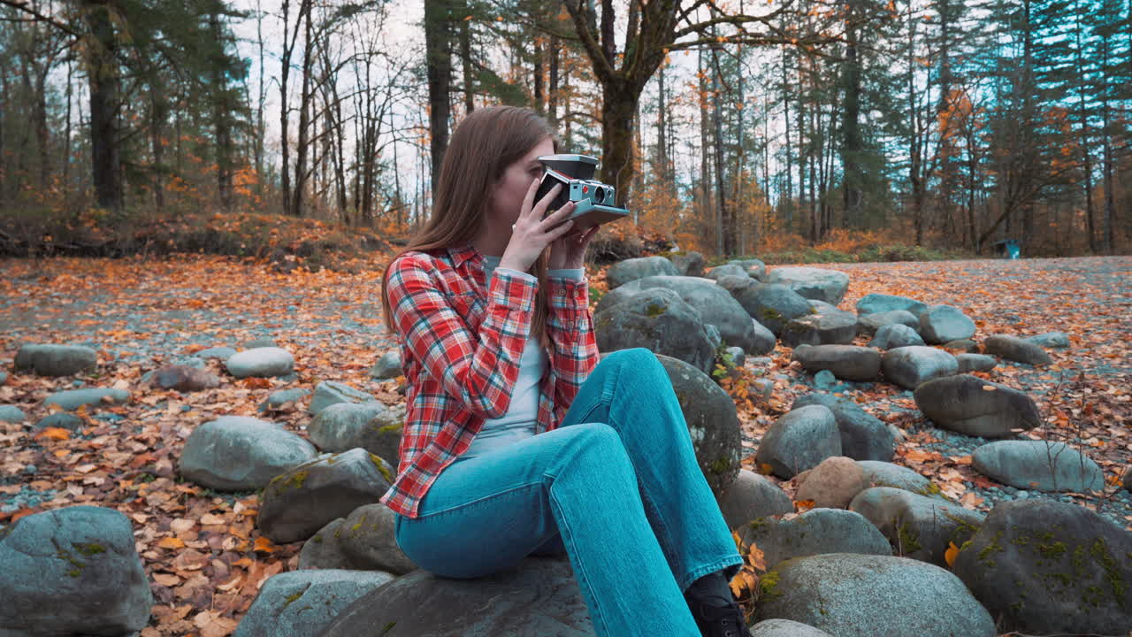 una mujer fotógrafa toma una foto polaroid a lo largo de la orilla del río entre los colores del otoño