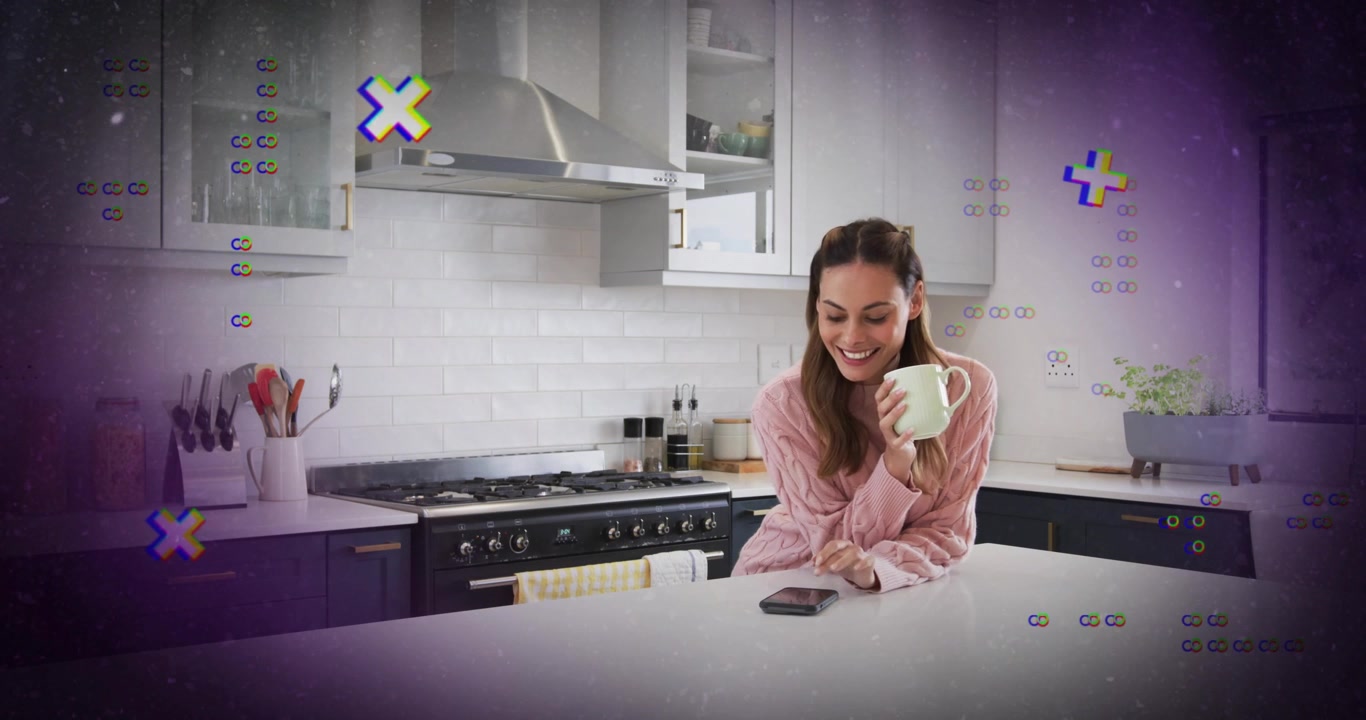 Donna che posiziona lo smartphone sull'isola della cucina, tenendo in mano una tazza, sentendo un "ping" che fa apparire un'icona di avviso tecnologico.