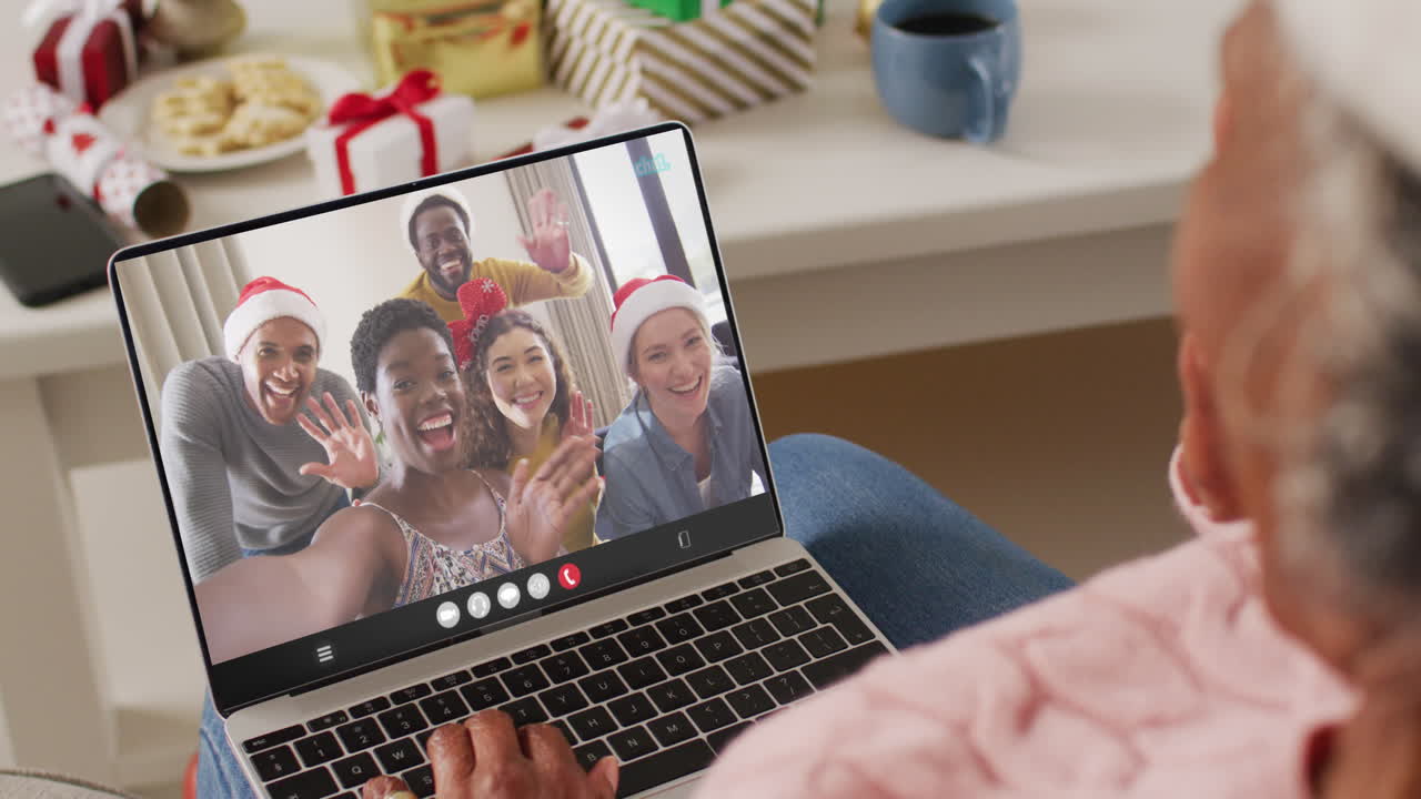 mujer afroamericana senior con sombrero de santa teniendo llamada de video portátil con amigos diversos felices