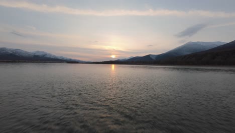 experience the tranquil beauty of nature as a drone captures the golden sun setting over a peaceful river, surrounded by majestic mountains
