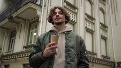 hombre feliz con café con leche sonriendo al aire libre. hombre alegre sosteniendo una taza de papel en la calle.