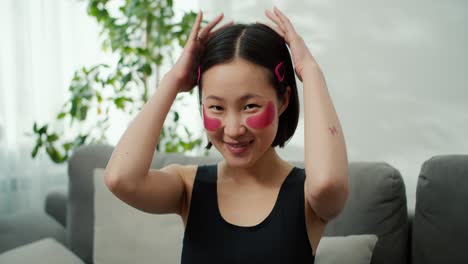 young asian woman with clear skin with moisturizing golden patches under her eyes sitting on the sofa in the living room