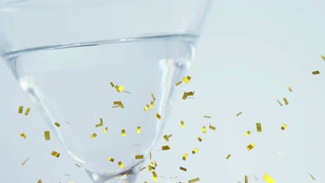 animation of gold confetti falling over into clear drink in glass, on white background