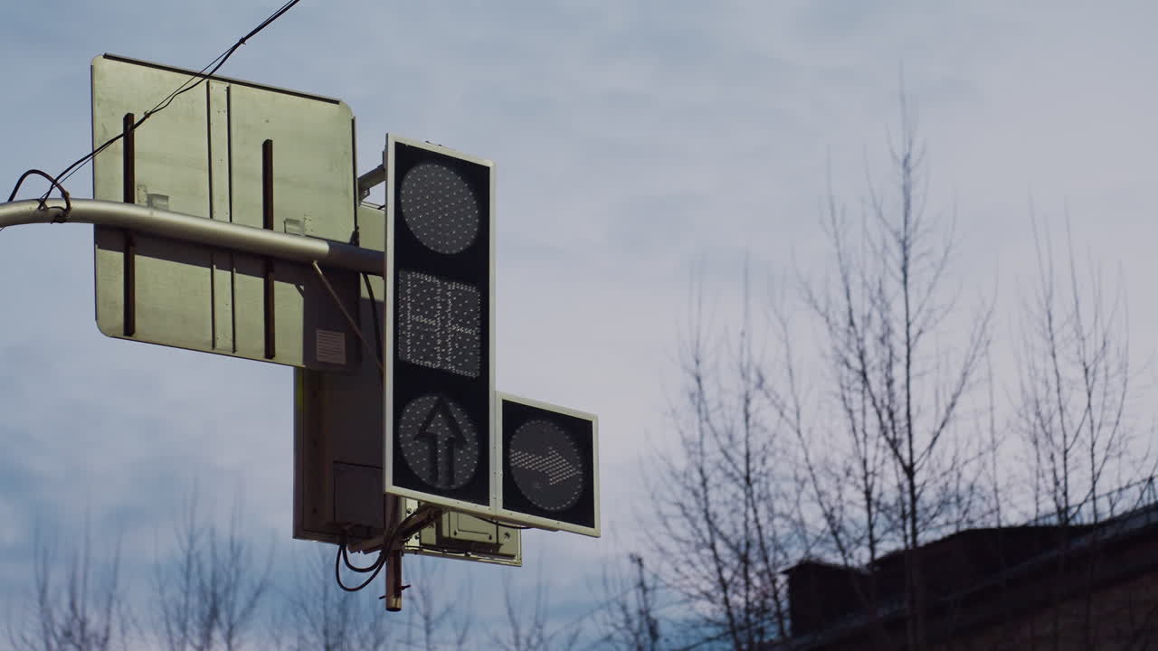 Traffic signal captured in transition mode showing off state after switching from green to red with arrow direction indicator inactive, silhouetted against daylight sky and bare tree branches