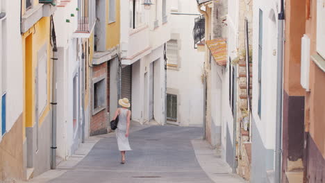 woman tourist in light dress and hat goes down the narrow streets of the old mediterranean city in s