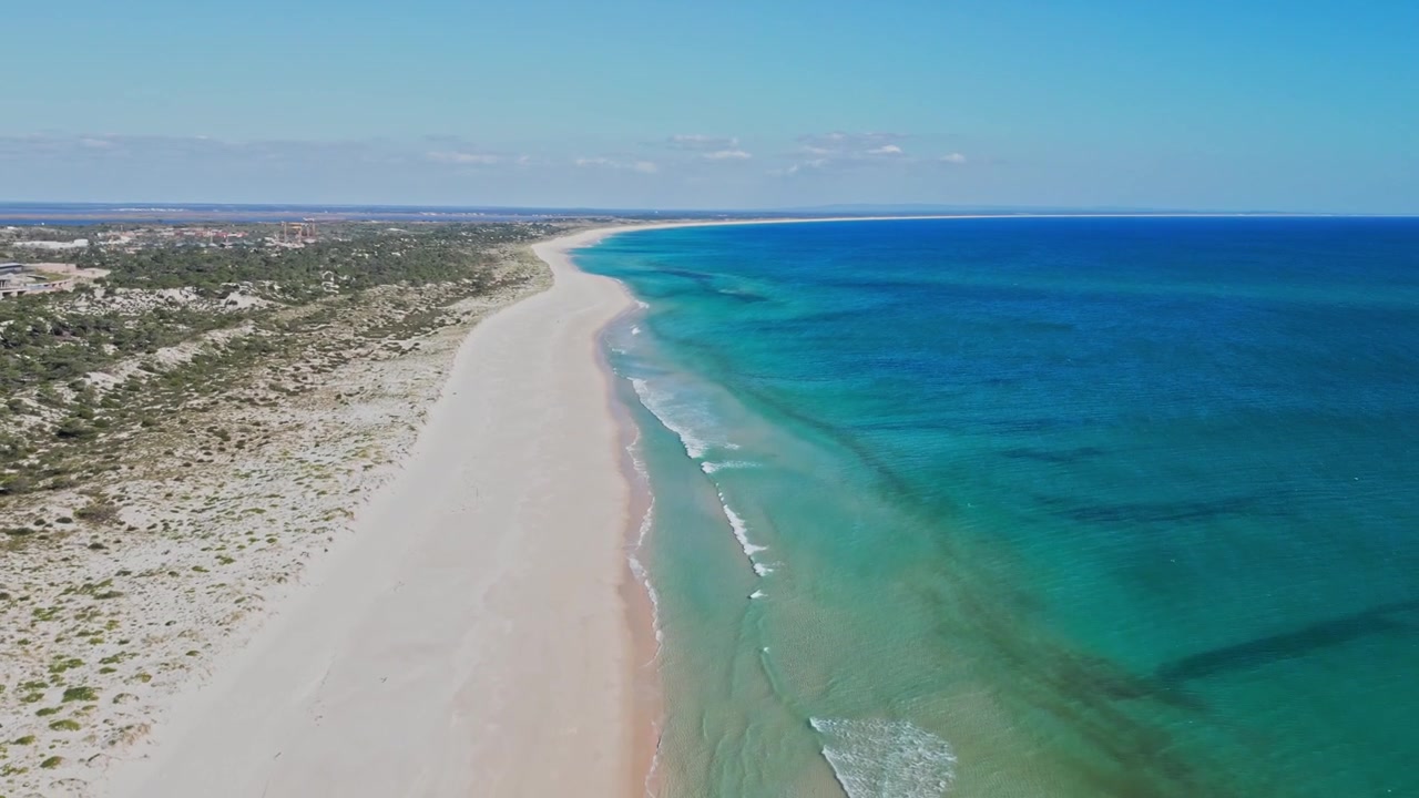 Ujęcie z lotu ptaka przemieszczające się wzdłuż opuszczonej piaszczystej plaży z turkusowym oceanem w słońcu