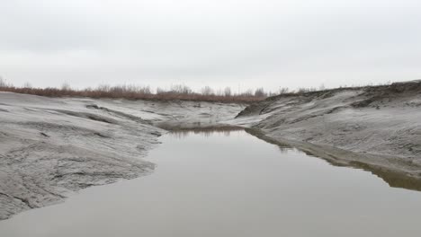 aerial push in over low tide muddy river bird flies by lands on water cloudy day