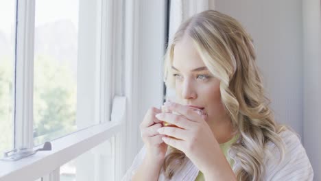 happy caucasian plus size woman looking through window and drinking tea in slow motion
