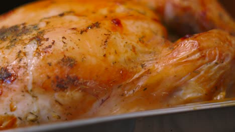 freshly roasted whole chicken in tray as camera moves along showing garlic herb seasoning on juicy meat.