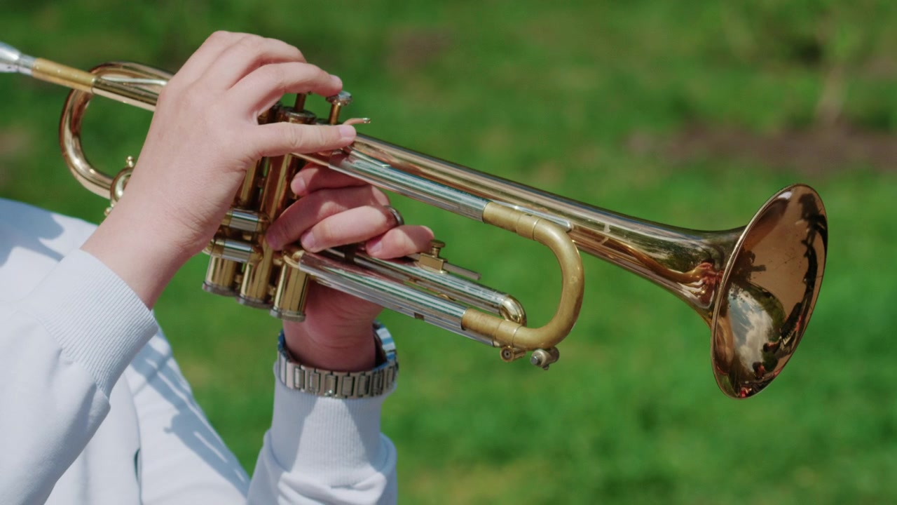 Primo piano delle mani di un musicista che premono le valvole della tromba mentre suona all'aperto.