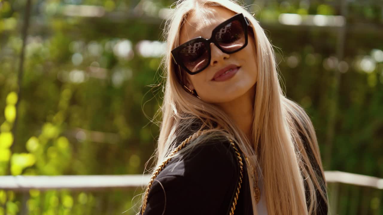 A beautiful blonde woman plays with her hair and sunglasses. She poses. Daylight in a beautiful park. close up, slow motion.