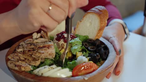 mujer comienza a comer ensalada de pollo a la parrilla fresca de un tazón de madera