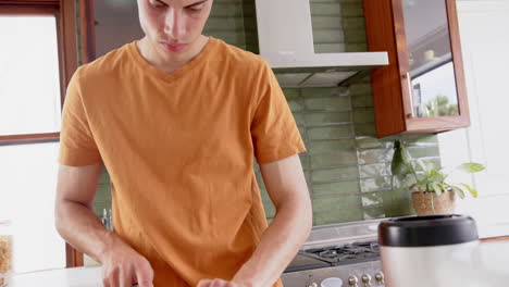 Focused-biracial-man-chopping-fruit,-preparing-healthy-smoothie-in-kitchen,-copy-space,-slow-motion