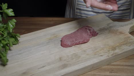 el chef agrega sal con las manos para saborizar el filete de carne de res en la tabla de madera de la cocina