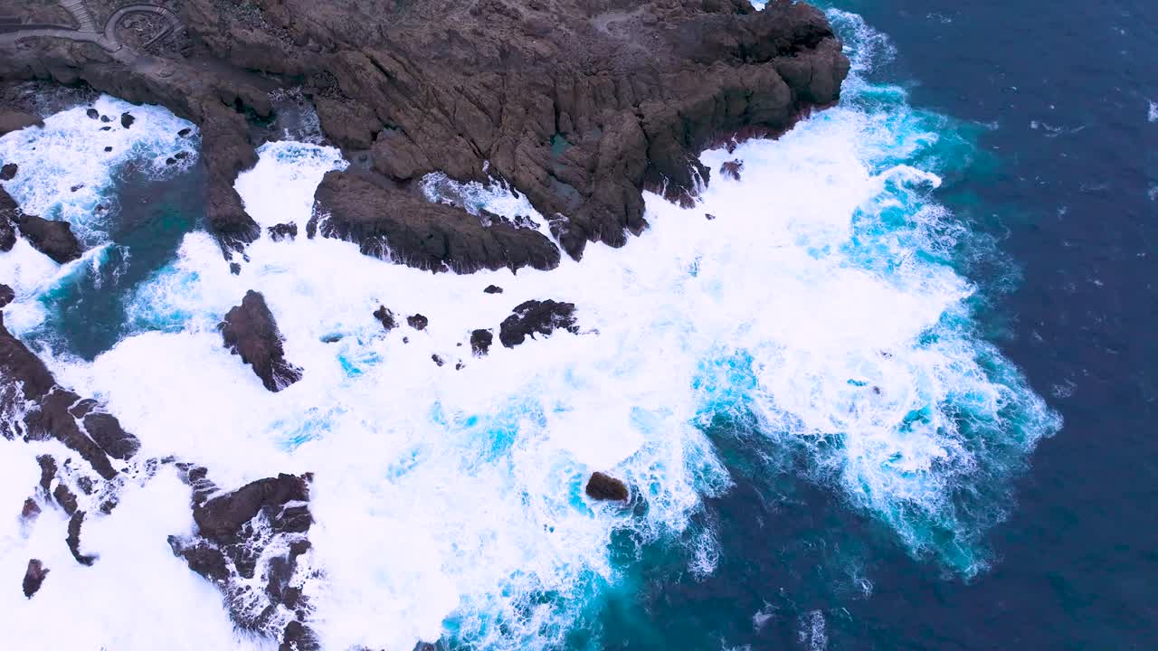 Choppy sea hitting volcanic rocks on Tenerife coast with foamy waves