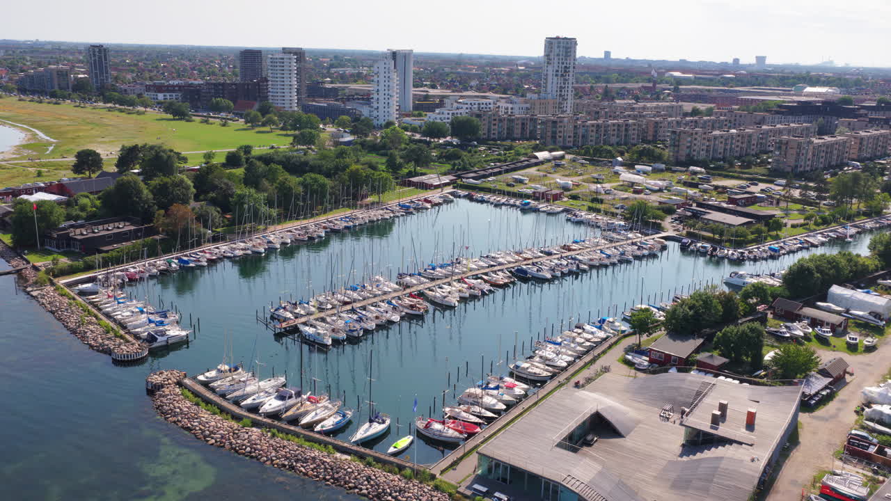 Aerial drone view of the marina filled with sailboats, surrounded by residential blocks and the green coast in Copenhagen, Denmark