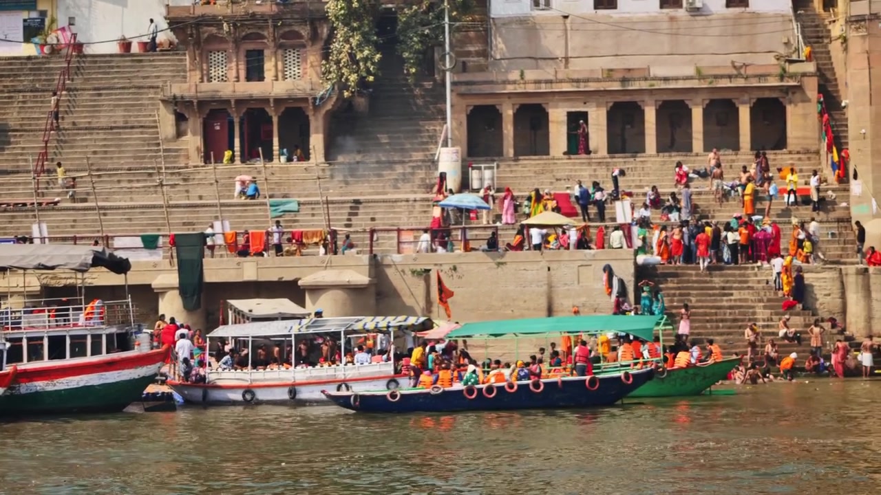 Banaras, Kashi, Varanasi, Uttar Pradesh, Hindistan'da tekneler ve turistlerle Tulsi Ghat. Gündüz, pan çekim, 4K