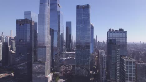 cinematic drone pull-out revealing the vessel and surrounding glass skyscrapers in hudson yards, new york city, with soft morning light and clear skies