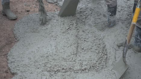 closeup of concrete being poured onto the ground while workers pave a street