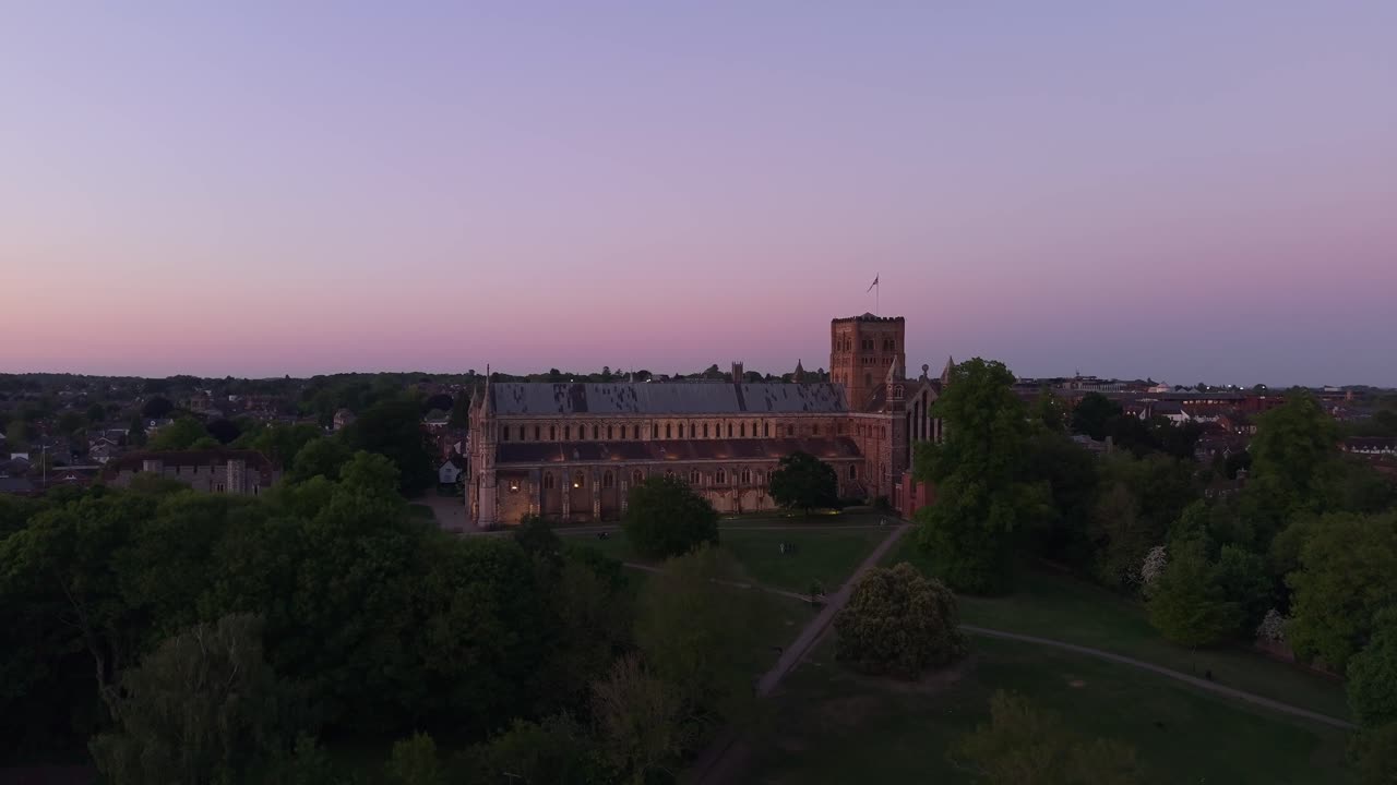A cinematic drone reveal shows the illuminated St Albans Cathedral glowing at the heart of the park during twilight, with a serene and atmospheric landscape