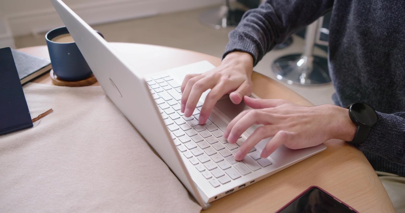 Uomo afroamericano che interrompe la digitazione al laptop, si allunga per sorseggiare da una tazza e poi riprende a scrivere.