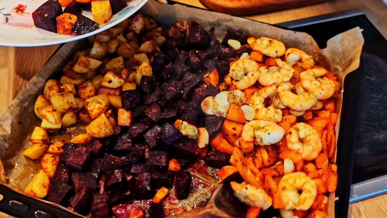 Colorful oven tray loaded with juicy garlic-herb shrimp, caramelized carrots, beets and potatoes being scooped onto a plate