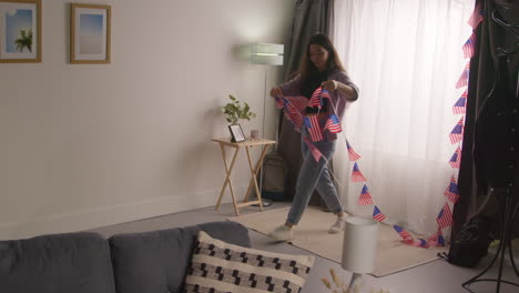 woman at home hanging up american stars and stripes flag bunting for party celebrating 4th july independence day