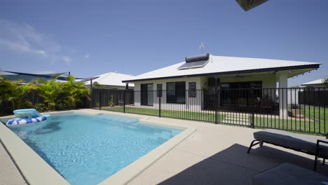 outdoor entertainment area, luxurious contemporary outdoor swimming pool in ground concrete decking, clear blue water black fence grey modern home green grass blue skies