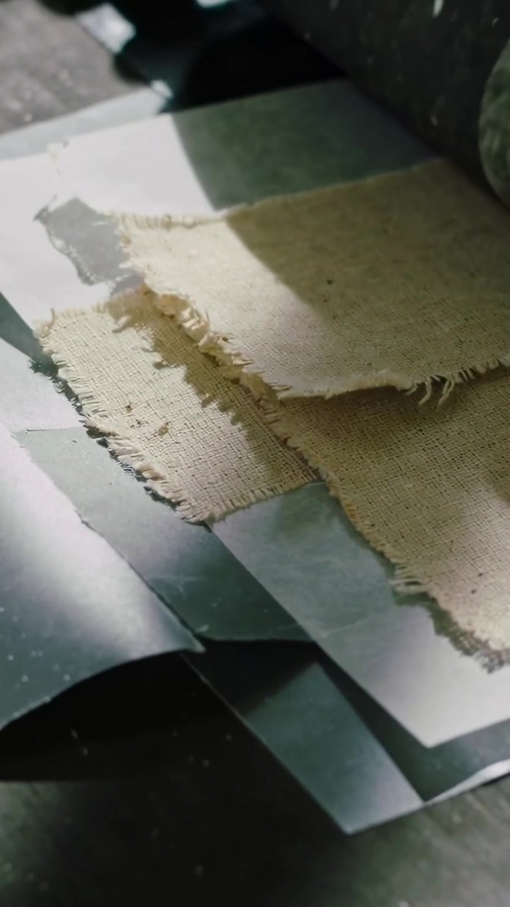 Vertical video: Roller entering top-right, rolling over frayed fabric on bench, gluing layers