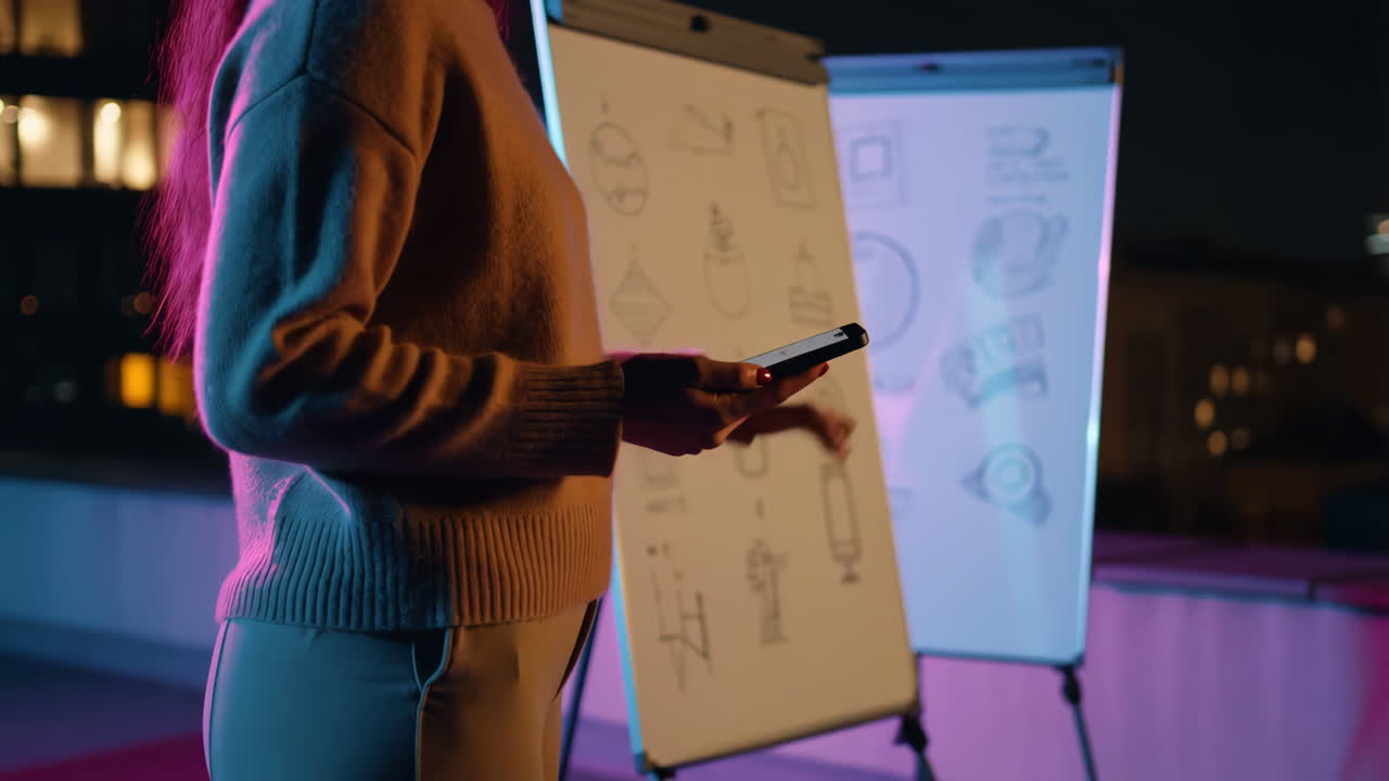 Person using a smartphone next to illuminated presentation boards at night