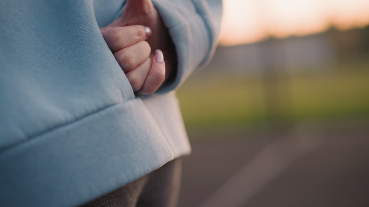 Close up of lady with polished nails brought to waist making hand gesture, blurred greenery in background, highlighting calm outdoor setting
