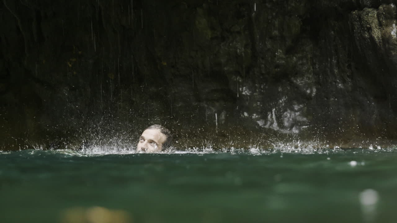 Man Swimming Under a Waterfall