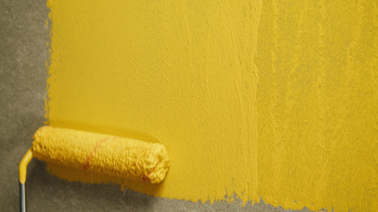Mano utilizando un rodillo para aplicar pintura amarilla en la pared