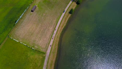 Aerial-view-of-several-people-riding-horses-along-a-rural-road-by-the-shore-of-a-lake